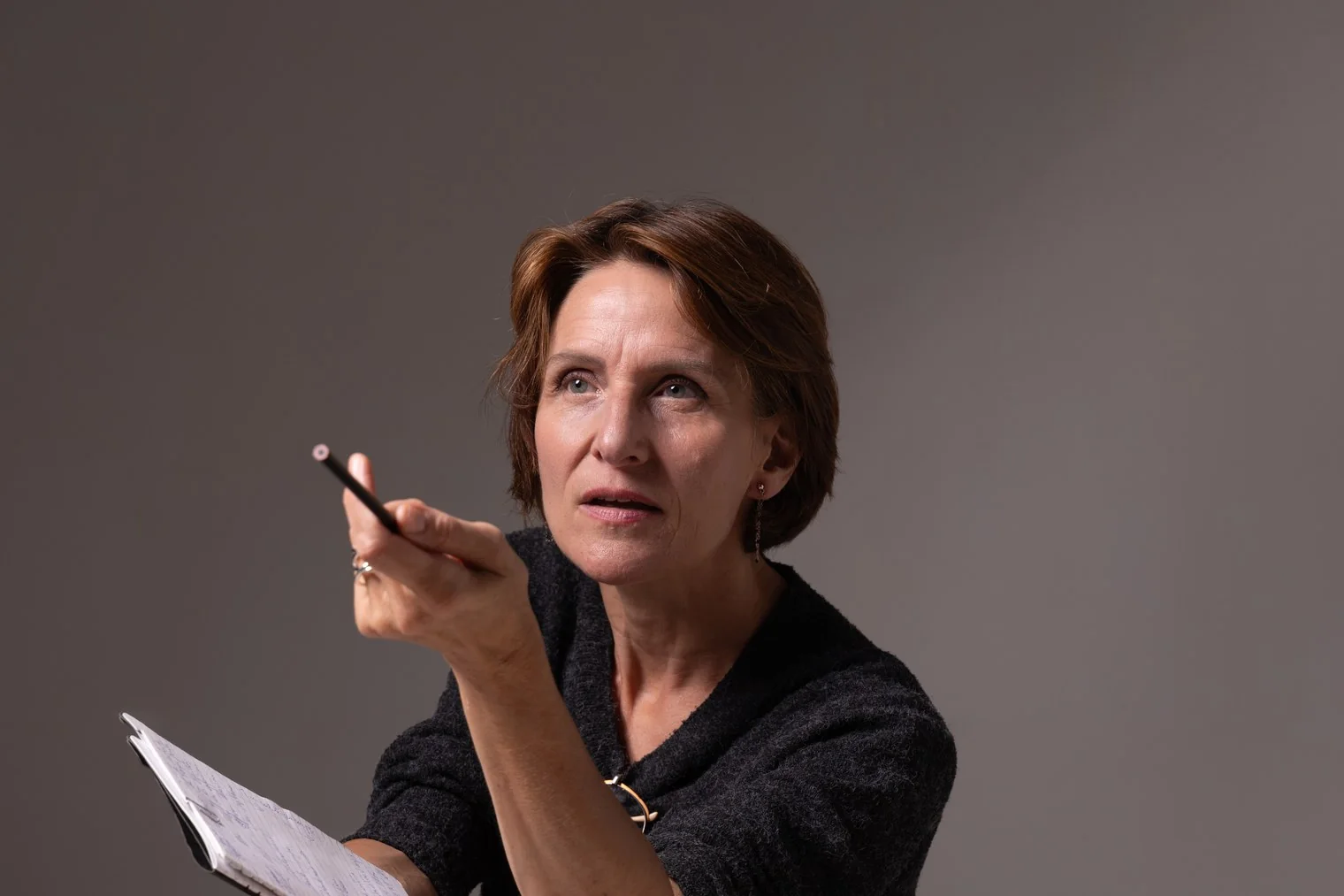 Laurence Arpi crayon et carnet en main, le regard levé, en séance de travail