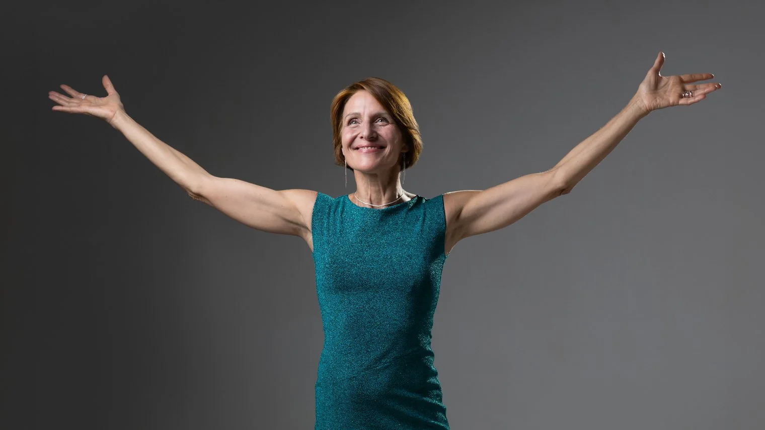Laurence Arpi en robe verte, bras grands ouverts, regard vers le haut