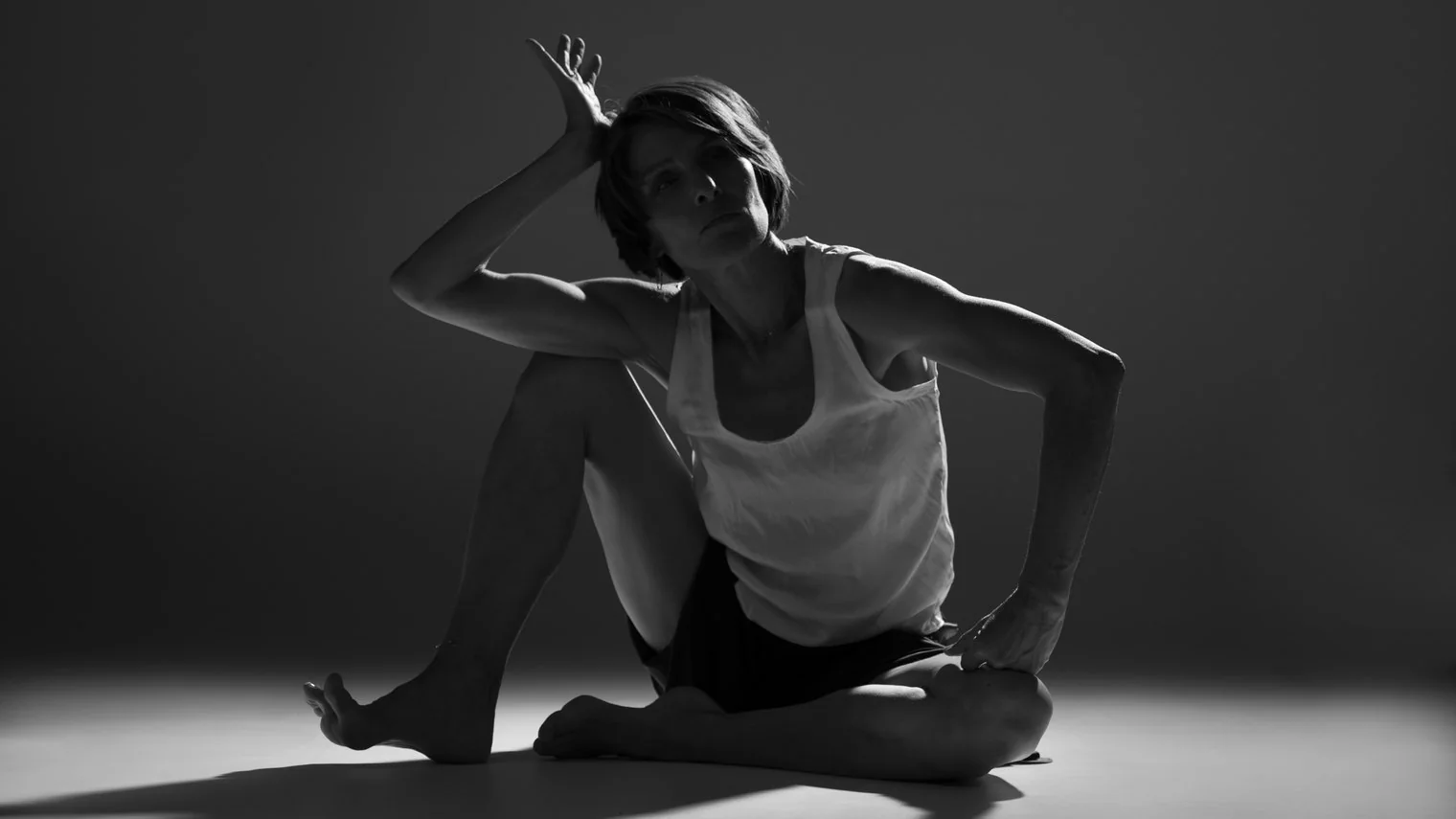 Laurence Arpi assise au sol, en appui sur une main, dans une lumière de studio en noir et blanc