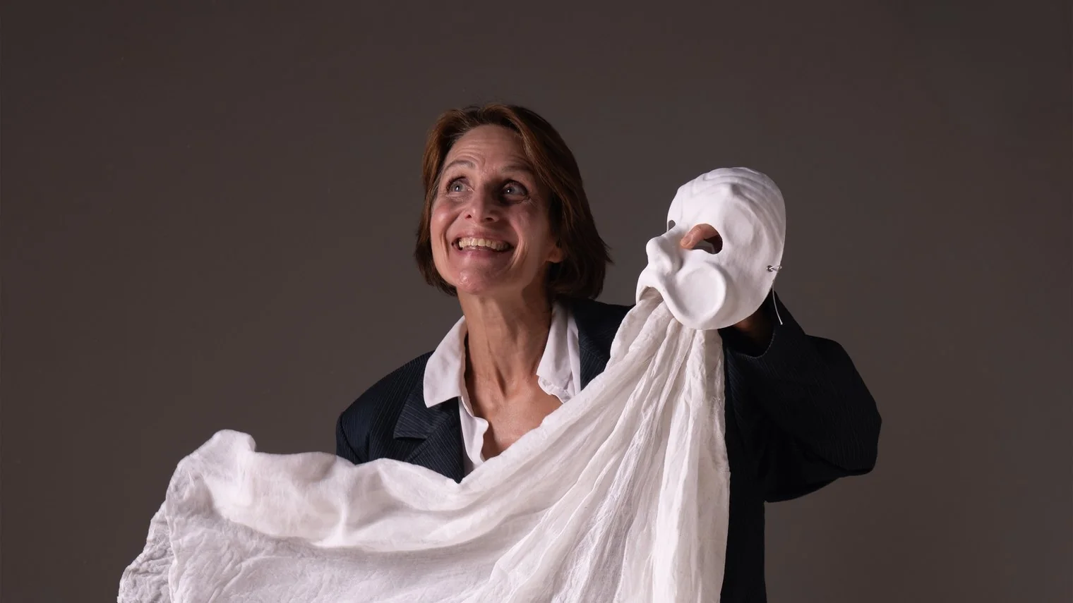Laurence Arpi tient un masque de théâtre blanc à bout de bras, le regard tourné vers lui