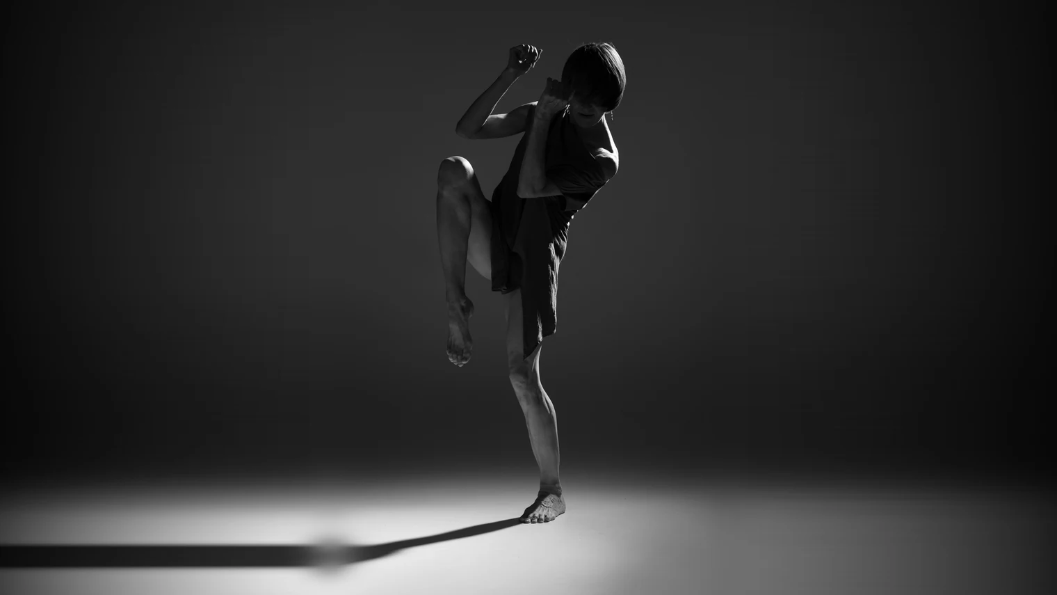 Laurence Arpi en training de théâtre physique, jambe levée en suspension, silhouette en noir et blanc dans la lumière du studio