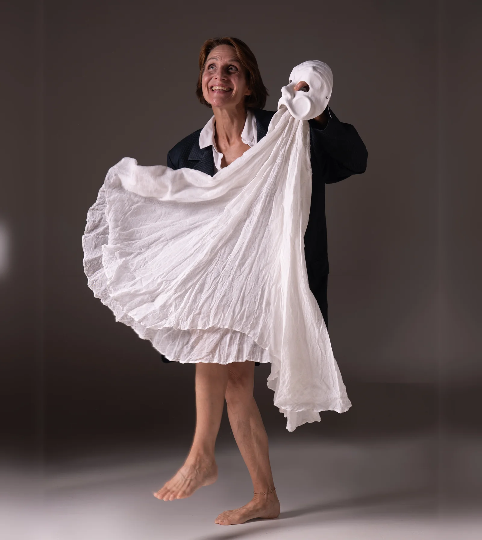 Laurence Arpi en scène, robe blanche déployée dans le mouvement, un masque de théâtre à la main