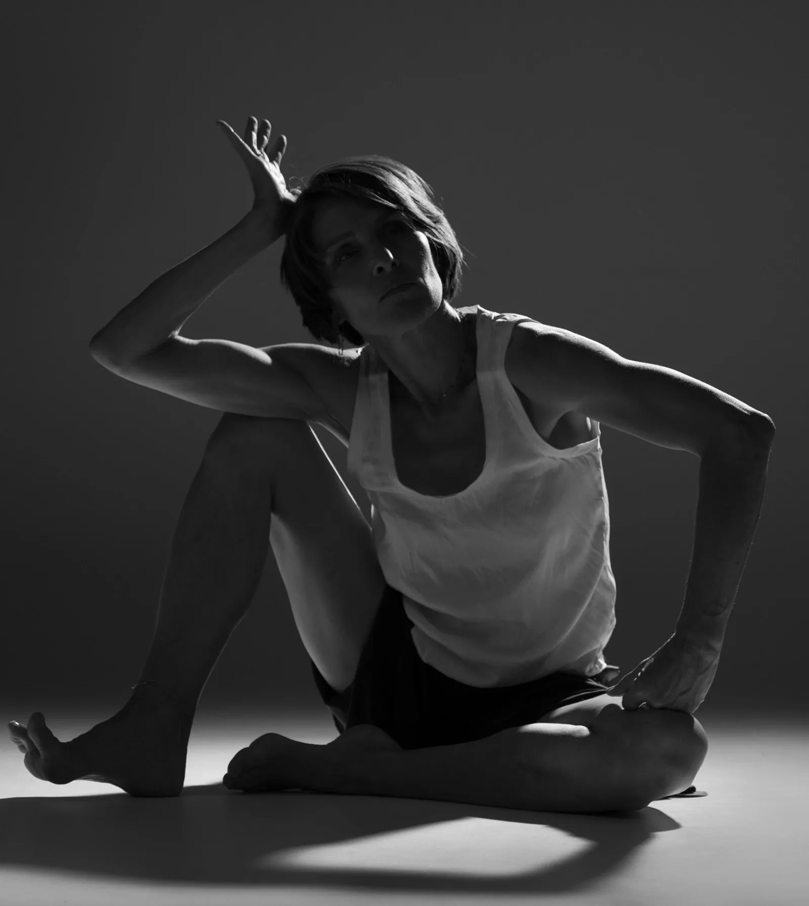Laurence Arpi assise au sol en travail de théâtre physique, noir et blanc sculpté par la lumière